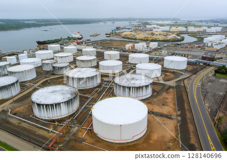 Numerous large storage tanks are situated crude oil near coast, surrounded by industrial activity ships in distance. Numerous large storage tanks are situated crude oil near coast, surrounded by industrial activity ships in distance. 128140696