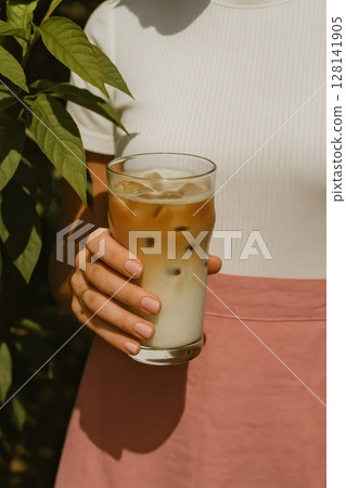 Woman in white top and pink skirt holds refreshing iced latte 128141905