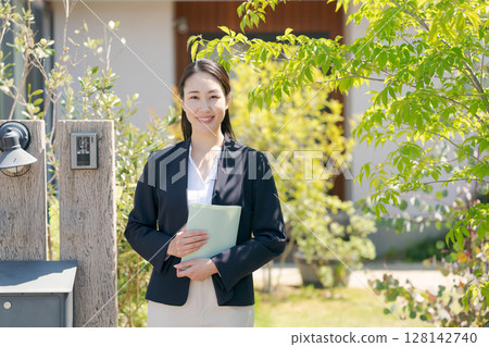 一位穿著西裝的女人站在一間房子前 一位穿著西裝的女人站在一間房子前 128142740