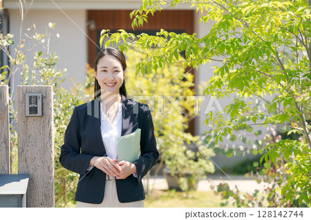 一位穿著西裝的女人站在一間房子前 128142744