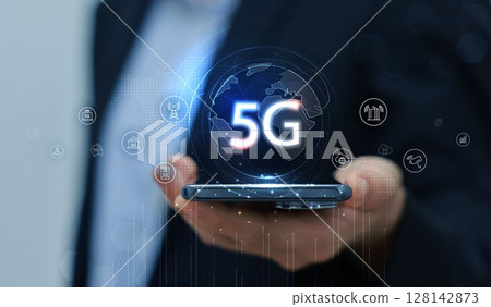 Hand holding smartphone with 5G icon and global network interface, representing high-speed wireless technology, digital connectivity, IoT, and future communication concept. communication network. Hand holding smartphone with 5G icon and global network interface, representing high-speed wireless technology, digital connectivity, IoT, and future communication concept. communication network. 128142873