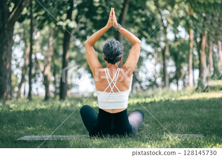 Mature Woman in Sukhasana with Urdhva Namaskarasana Pose Outdoors in Tranquil Forest Setting Mature Woman in Sukhasana with Urdhva Namaskarasana Pose Outdoors in Tranquil Forest Setting 128145730