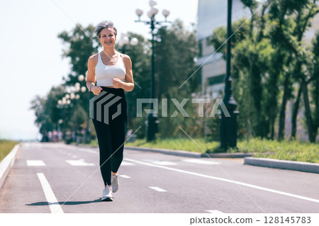 Confident Mature Woman Jogging Outdoors on a Sunny Day in Sportswear and Smartwatch Confident Mature Woman Jogging Outdoors on a Sunny Day in Sportswear and Smartwatch 128145783