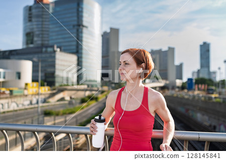 Woman resting after her morning workout, drinking water on a city bridge Woman resting after her morning workout, drinking water on a city bridge 128145841