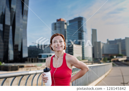 Woman resting after her morning workout, drinking water on a city bridge 128145842