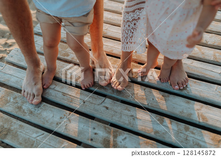 Legs and feet of family standing on beach on wooden walkway. 128145872