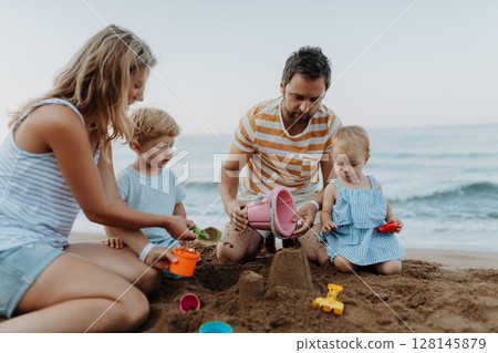 Two toddler children playing on sand beach with paretns during summer holiday. Two toddler children playing on sand beach with paretns during summer holiday. 128145879