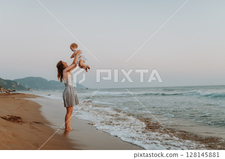 Side view of mom playing with baby daughter on sunny beach. Side view of mom playing with baby daughter on sunny beach. 128145881
