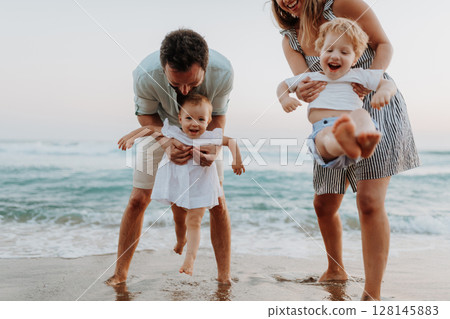 A young family with two toddler children having fun on beach on summer holiday. 128145883