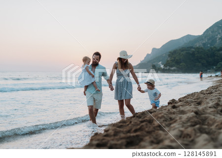 A family with two toddler children walking on beach on summer holiday at sunset. A family with two toddler children walking on beach on summer holiday at sunset. 128145891