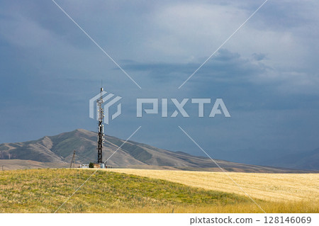 Telecommunication tower on hill, near agricultural field. Countryside landscape 128146069