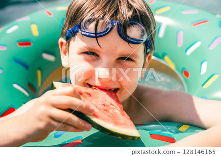 Smiling boy biting watermelon slice in pool float on sunny summer day, close-up portrait fun Smiling boy biting watermelon slice in pool float on sunny summer day, close-up portrait fun 128146165