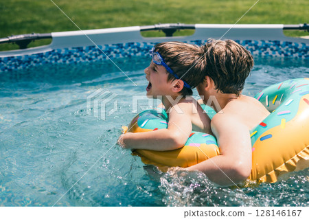 Boys laughing and playing in the pool with colorful inflatable donut ring on sunny summer day Boys laughing and playing in the pool with colorful inflatable donut ring on sunny summer day 128146167