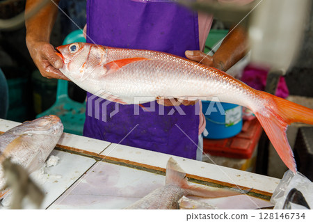 Fresh red snapper held by fish vendor at wet market in Philippines with cutting table and seafood in background 128146734