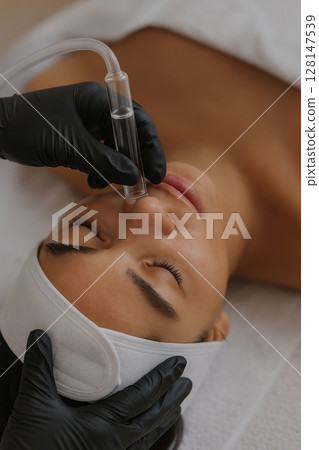 Woman receiving professional hydrafacial treatment with vacuum suction on nose Woman receiving professional hydrafacial treatment with vacuum suction on nose 128147539
