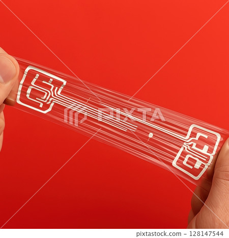 Hands stretching transparent flexible electronic circuit with printed conductive lines  128147544