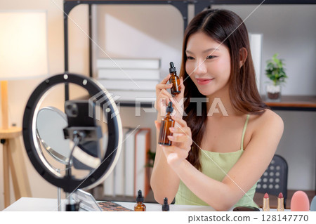 Young asian woman demonstrating serum on hands on social media at home, skincare and cosmetic. 128147770