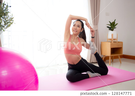 Young asian woman practicing Yoga with stretching muscle back on yoga mat in living room. Young asian woman practicing Yoga with stretching muscle back on yoga mat in living room. 128147771
