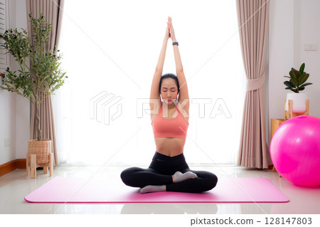 Young asian woman meditation sitting on mat in serene and tranquility with yoga in living room. Young asian woman meditation sitting on mat in serene and tranquility with yoga in living room. 128147803