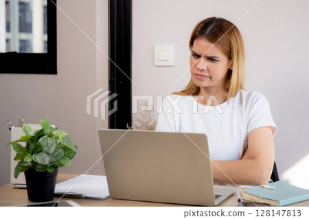 Unhappy young caucasian businesswoman using laptop computer on desk with stress and burnout. 128147813