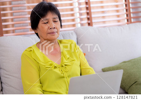 Asian senior woman sitting on sofa using laptop computer for looking social media in living room. Asian senior woman sitting on sofa using laptop computer for looking social media in living room. 128147821