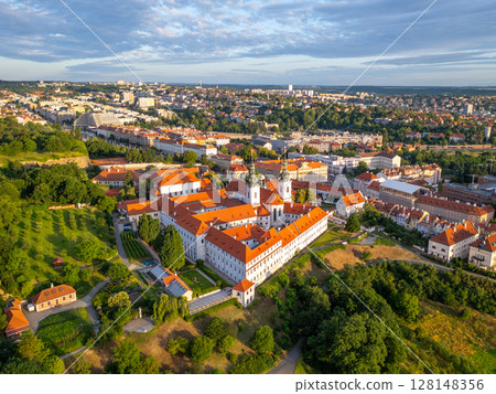 Aerial view of Strahov Monastery reveals stunning architecture bathed in the soft light of sunrise, surrounded by lush greenery and the vibrant skyline of Prague. Aerial view of Strahov Monastery reveals stunning architecture bathed in the soft light of sunrise, surrounded by lush greenery and the vibrant skyline of Prague. 128148356