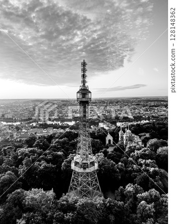 At sunrise, the Petrin Lookout Tower stands tall above the city of Prague, surrounded by lush greenery. The bright sky casts stunning colors over the landscape, creating a breathtaking view. At sunrise, the Petrin Lookout Tower stands tall above the city of Prague, surrounded by lush greenery. The bright sky casts stunning colors over the landscape, creating a breathtaking view. 128148362