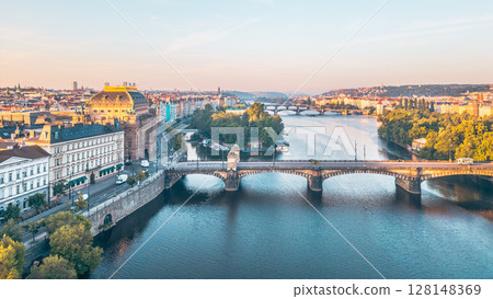 Aerial view of the Vltava River winding through Prague at sunset, showcasing the National Theatre. Diverse architecture and lively atmosphere reflect the city's charm and history. Aerial view of the Vltava River winding through Prague at sunset, showcasing the National Theatre. Diverse architecture and lively atmosphere reflect the city's charm and history. 128148369