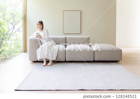 Woman sitting on a sofa and looking at a smartphone Woman sitting on a sofa and looking at a smartphone 128148521