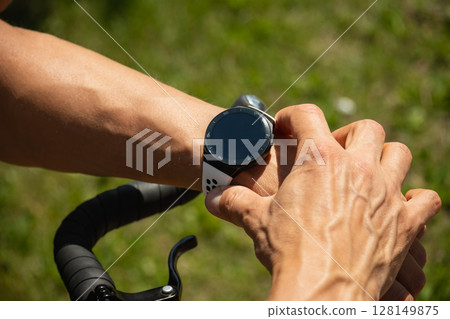 Athlete cyclist checking distance, pulse or fitness progress in apps after riding. Close up man hands checking his heartbeat with smartwatch. Summer activity. 128149875
