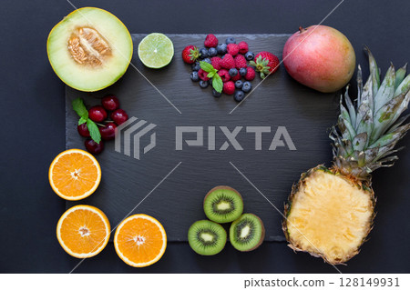 Rectangle from laid out fruit pineapple, mango, kiwi, oranges, lime, melon and berries cherries, strawberries, blueberries, raspberries in middle copy space on black background. Top view, flat lay 128149931