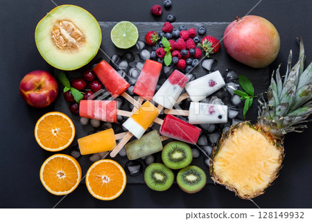 In the center on ice cubes variety of sorbet and ice cream cones near ingredients fruits and berries on black background. Summer coolness of ice cream and sorbet cones. Horizontal. Top view. 128149932