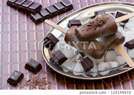Melted chocolate ice cream sits on a silver plate surrounded by ice and chunks of chocolate. 128149939