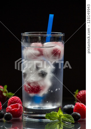 Chilled glass of iced water filled with fresh berries and ice cubes sits against a dark backdrop, providing a refreshing drink option for a hot summer day. Chilled glass of iced water filled with fresh berries and ice cubes sits against a dark backdrop, providing a refreshing drink option for a hot summer day. 128149943