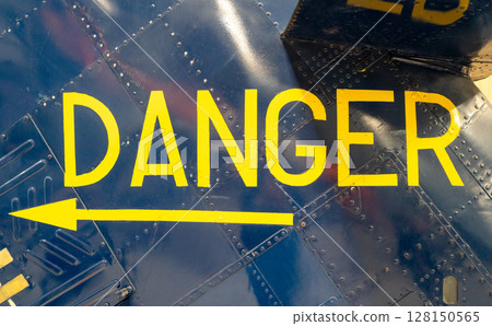 Yellow -Danger- warning sign on blue metallic aircraft fuselage panel 128150565
