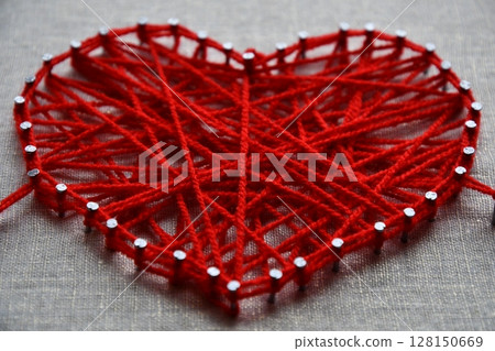 Red heart string art made with tangled yarn on metal nails on canvas background 128150669
