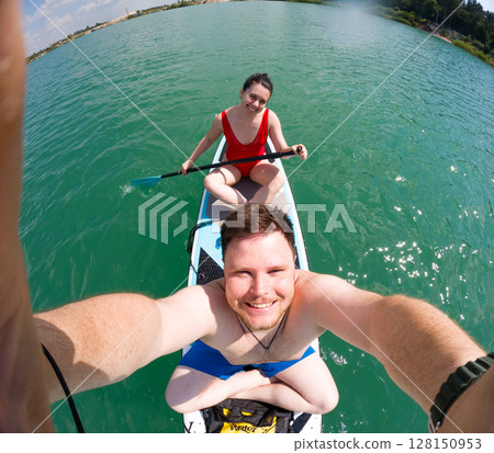 Couple Paddleboarding on a Sunny Lake Couple Paddleboarding on a Sunny Lake 128150953