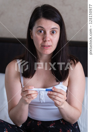 Woman Holding Positive Pregnancy Test with Worried Expression 128150977