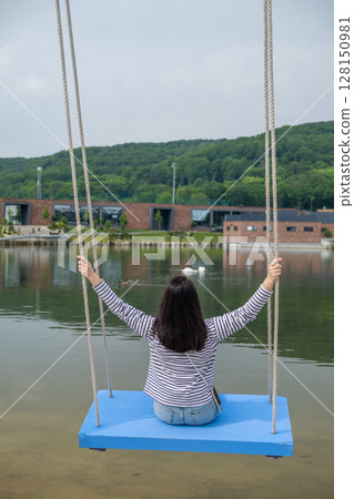 Person Relaxing on Swing by Scenic Lake 128150981
