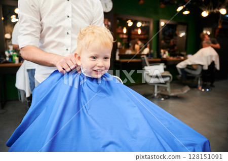 Adorable kid excited about new haircut. Little boy first time in barbershop. Cute client waiting for hairdresser. 128151091