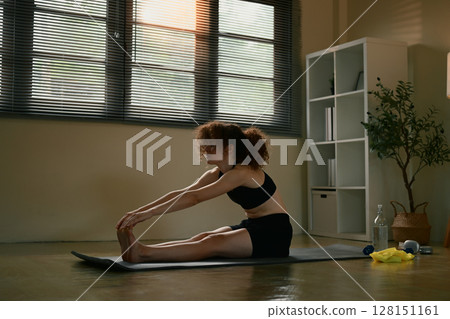 Fit young woman practicing yoga and stretching legs during a morning workout session 128151161