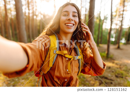Beautiful woman taking picture of herself while walking in sunny forest. Selfie in nature. Adventure 128151162