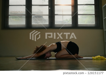 Young woman in sportswear stretching and unwinding in a serene home exercise Young woman in sportswear stretching and unwinding in a serene home exercise 128151177