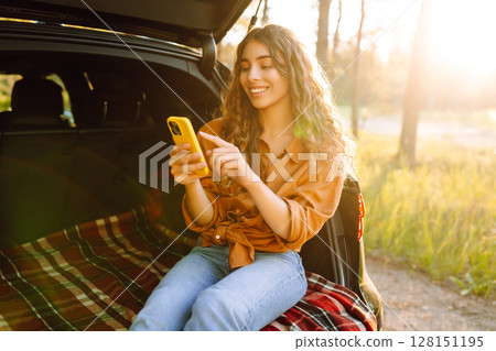 Young woman enjoys a sunny day outdoors while sitting in her car. Travel, weekend, nature, relax 128151195
