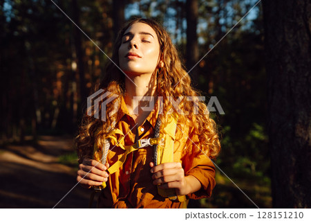 Tourist woman hiking alone in thick autumn forest. Stylish female looks for pathway among trees. Tourist woman hiking alone in thick autumn forest. Stylish female looks for pathway among trees. 128151210