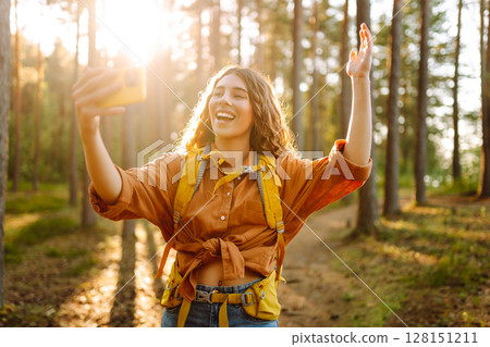 Beautiful woman taking picture of herself while walking in sunny forest. Selfie in nature. Adventure Beautiful woman taking picture of herself while walking in sunny forest. Selfie in nature. Adventure 128151211