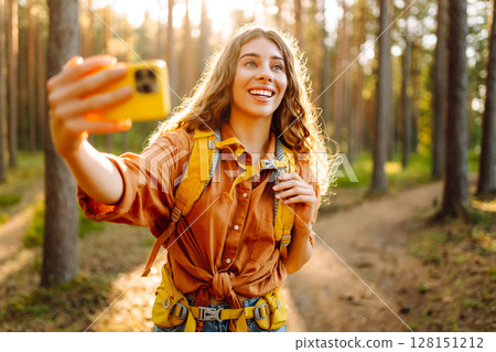 Beautiful woman taking picture of herself while walking in sunny forest. Selfie in nature. Adventure Beautiful woman taking picture of herself while walking in sunny forest. Selfie in nature. Adventure 128151212