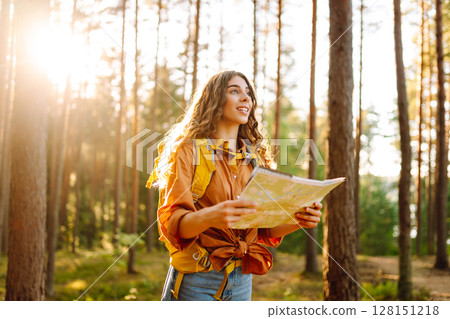 A traveler woman stands in a lush forest, examining a map with a focused expression A traveler woman stands in a lush forest, examining a map with a focused expression 128151218