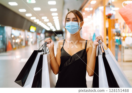Fashionable woman in protective medical mask with shopping bags walking in the mall. Covid-19. Fashionable woman in protective medical mask with shopping bags walking in the mall. Covid-19. 128151488