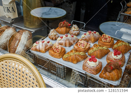 Danish pastry on a a cafe showcase behind the window: view from the street. Tasty buns and croissants in a bakery in Copenhagen, Denmark Danish pastry on a a cafe showcase behind the window: view from the street. Tasty buns and croissants in a bakery in Copenhagen, Denmark 128151594